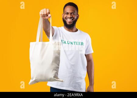 African Volontario uomo mostrando Eco Bag a macchina fotografica, sfondo giallo Foto Stock