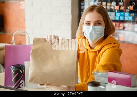 Il ritratto del lavoratore della cucina emette gli ordini in linea nei guanti e nella maschera. Take-away sacchetto di carta alimentare mock up. Confezione di sacchetti per il cibo da portare nella mensa da asporto Foto Stock