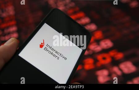 Viersen, Germania - 6 febbraio. 2021: Primo piano dello schermo del telefono cellulare con la scritta del logo dei mediatori interattivi, sfondo della tabella del mercato azionario Foto Stock