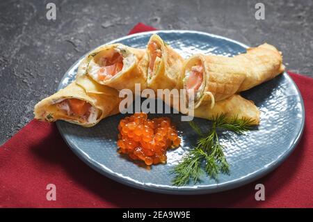 Deliziosa colazione - crepes con salmone affumicato, panna acida e caviarca su fondo di pietra nera. Foto Stock