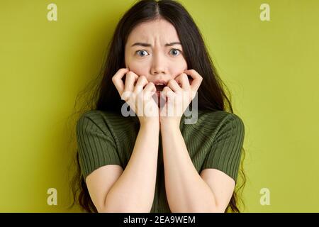 spaventata donna in piedi nella paura di tenere le mani vicino al viso, guardando la macchina fotografica orribile da qualcosa è accaduto. isolato sfondo verde studio Foto Stock