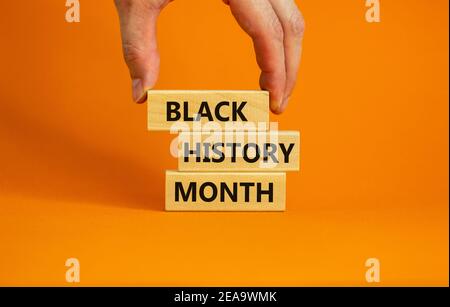 Simbolo del mese della storia nera. Blocchi di legno con parole 'mese della storia nera'. Bellissimo sfondo arancione. Mano dell'uomo. Storia nera concetto mese. Copia s Foto Stock