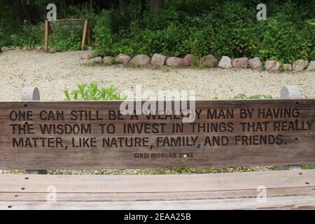 Una panchina di parco in legno con citazione incisa di Cindi Morgan Dyke circondata da un sentiero alberato ai Giardini Botanici Rotary a Janesville, Wisc Foto Stock