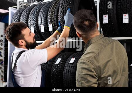 il venditore offre nuove ruote in gomma, pneumatici, cerchioni per l'auto. cliente maschile è venuto a fare l'acquisto nel negozio di servizio auto. meccanico auto mostrando l'assortimento Foto Stock
