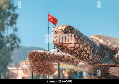 Famoso monumento a testa di loggerhead Caretta tartaruga di mare che depone uova nella sabbia sulla spiaggia con bandiera turca sullo sfondo. Il delta del fiume Dalyan è un nat Foto Stock