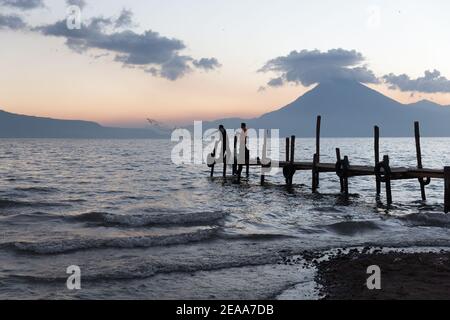Panajachel, Lago Atitlan Guatemala Lago Atitlan al tramonto. I pescatori gettano le reti su un molo con il vulcano San Pedro in lontananza. Foto Stock