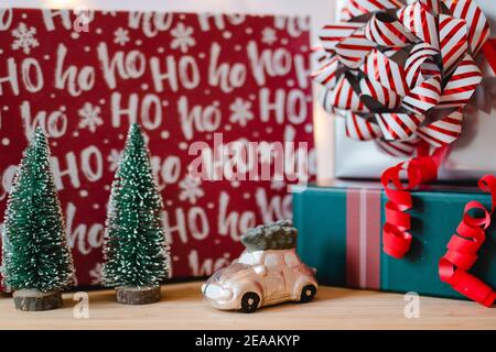 Decorazione di Natale con regali in scatole, piccoli abeti, cervi decorazione e auto con albero sul tetto di fronte a una tenda di luci, umore romantico Foto Stock