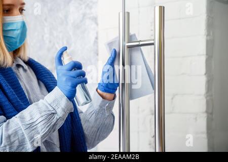 Donna Houseworker ritratto in gomma blu guanti pulire manopola porta con panno. Pulire la maniglia della porta anteriore con uno spray antibatterico imbevuto di alcool. Nuovo normale Foto Stock