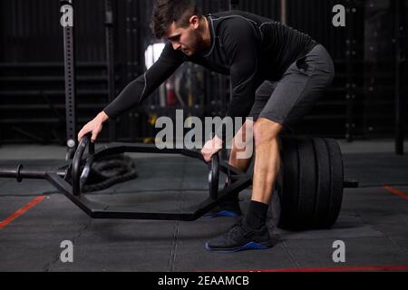 sportivo che muove pesi o crossbar in palestra, cambio attrezzatura, stand che tiene barbell, giovane maschio che va ad esercizi con attrezzature sportive, allenamento Foto Stock