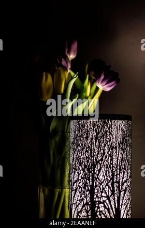 tulipani gialli e viola in un vaso dietro una lampada con un motivo di foresta Foto Stock