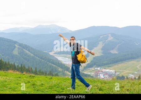 Un ragazzo viaggia con uno zaino giallo attraverso luoghi pittoreschi con splendidi paesaggi di montagna. Foto Stock