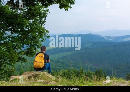 Solo ragazzo seduto sulla scogliera e godere di un tranquillo paesaggio verde montagne. Tranquillità e relax. Foto Stock