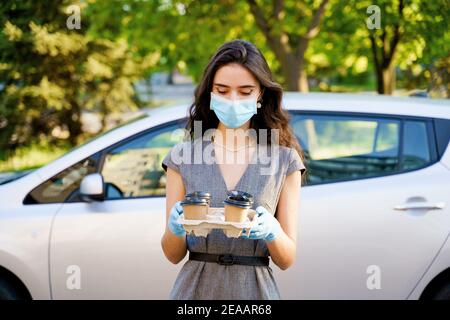 Consegna in auto del caffè dalla caffetteria. Cocee in tazza di cartone eco-usa e getta. Giovane ragazza lavora in agenzia di consegna e consegna caffè in auto. 4 co Foto Stock