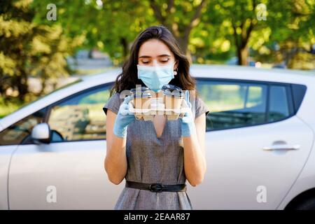 Consegna in auto del caffè dalla caffetteria. Cocee in tazza di cartone eco-usa e getta. Giovane ragazza lavora in agenzia di consegna e consegna caffè in auto. 4 co Foto Stock