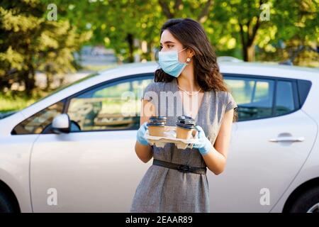 Consegna in auto del caffè dalla caffetteria. Cocee in tazza di cartone eco-usa e getta. Giovane ragazza lavora in agenzia di consegna e consegna caffè in auto. 4 co Foto Stock