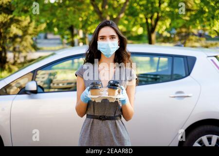 Consegna in auto del caffè dalla caffetteria. Cocee in tazza di cartone eco-usa e getta. Giovane ragazza lavora in agenzia di consegna e consegna caffè in auto. 4 co Foto Stock