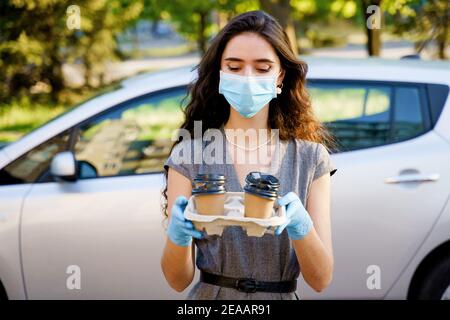 Consegna in auto del caffè dalla caffetteria. Cocee in tazza di cartone eco-usa e getta. Giovane ragazza lavora in agenzia di consegna e consegna caffè in auto. 4 co Foto Stock