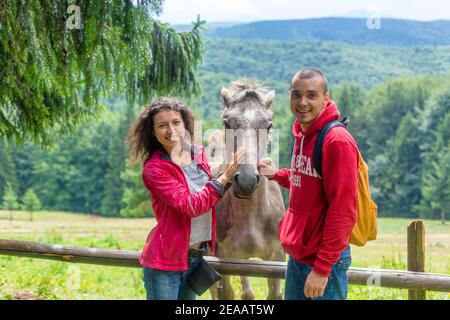 Coppia che accarezzano il cavallo su recinto di legno in terreni agricoli altipiani. Foto Stock