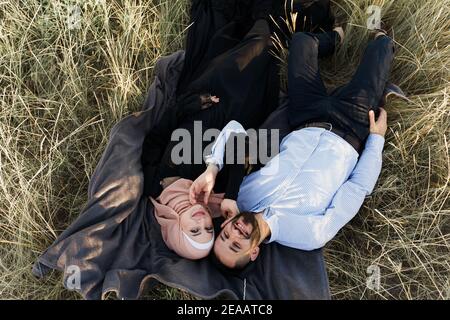 Storia d'amore musulmana. La coppia mista si stende sull'erba, sorrisi e abbracci. La donna si strappare in hijab guarda al suo uomo. Annuncio per l'agenzia di incontri on-line Foto Stock