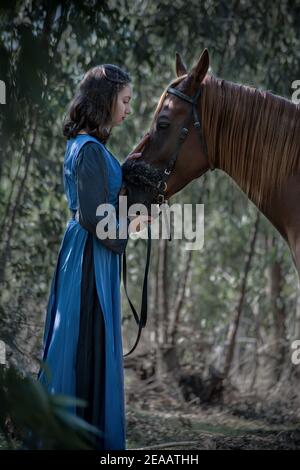 Profilo di una giovane ragazza carezzando dolcemente un cavallo con un aspetto affettuoso, mentre sono nel bosco su una luce bluastra mattina. Foto Stock