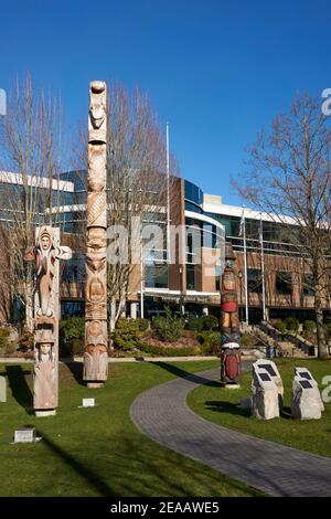 Kwakiutl stile riconciliazione totem pole e Coast Salish Welcome Posts al di fuori del Vancouver School Board edificio, Vancouver, BC, Canada Foto Stock