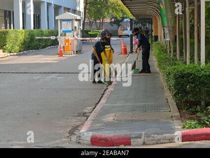 Bangkok, Thailandia - 2 febbraio 2021 : le lavoratrici femminili stanno spazzando strada e marciapiede usando scopa e casseruole, le scopa sono in movimento sfocato Foto Stock