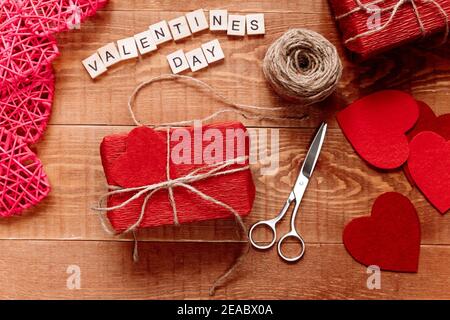 Un regalo fatto a mano avvolto in carta corrugata giace su un tavolo di legno. San Valentino Foto Stock