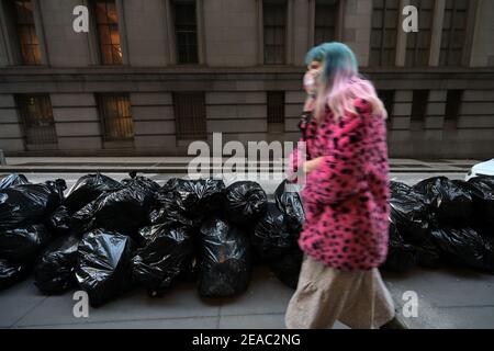 New York, Stati Uniti. 8 febbraio 2021. Una donna passa accanto a un mucchio di sacchi di spazzatura non raccolti a Lower Manhattan, dopo che due tempeste di neve hanno colpito New York in una settimana, 8 febbraio 2021. Il Department of Sanitation of New York sta riprendendo la raccolta dei rifiuti dopo aver incaricare i suoi dipendenti e camion per arare la neve nei cinque quartieri di New York City. (Foto di Anthony Behar/Sipa USA) Credit: Sipa USA/Alamy Live News Foto Stock