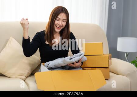 donna allegra aprire scatola di cartone nel soggiorno a casa, acquistare sul negozio online Foto Stock