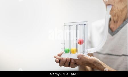 La vecchia mano del paziente che tiene la spirometria di incentivo Tri-ball è un'apparecchiatura medica per il post-funzionamento. L'apparecchiatura per il test di funzionamento dei polmoni & il Pul Foto Stock