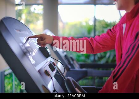 Una donna che si allenava in palestra su un tapis roulant, raggiungendo il monitor touch screen per modificare l'impostazione della velocità. Foto Stock