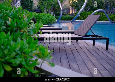 Vista sulla piscina con file di sedie in legno reclinabili sul bordo di una piscina con acqua blu chiaro al mattino. Foto Stock