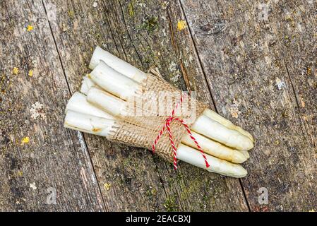 Diversi gambi di asparagi legati insieme con una corda rossa su una superficie di legno resistente alle intemperie Foto Stock