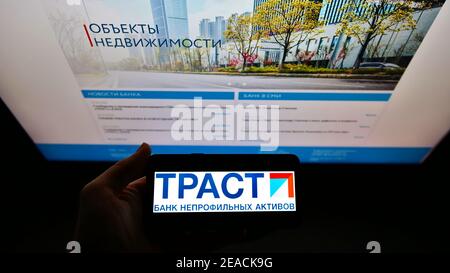Persona che detiene smartphone con il logo della società russa National Bank Trust (ТРАСТ) sullo schermo con il sito Web aziendale. Mettere a fuoco il display del telefono. Foto Stock