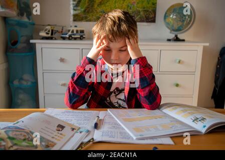 Un ragazzo si siede alla sua scrivania in homeschooling facendo i chores per la scuola. Foto Stock