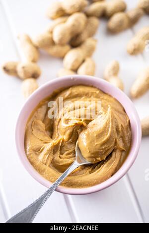 Burro di arachidi in recipiente e arachidi su tavola bianca. Foto Stock