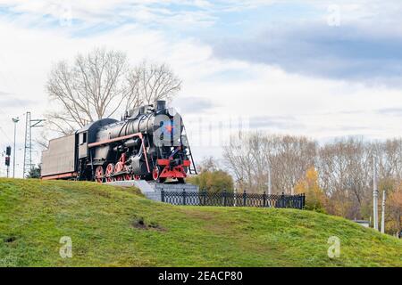 Vecchio treno d'epoca sovietico, locomotiva a vapore con una stella rossa si erge su un piedistallo come monumento, un punto di riferimento della città Foto Stock