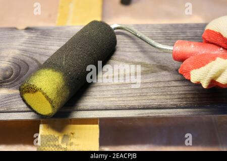Manipolazione di una tavola di legno di pino con una macchia scura usando un rullo di schiuma. Falegnameria e lavori di pittura. Foto Stock
