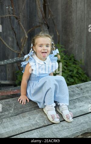 Carino ragazza divertente in un vestito blu è seduto nel cortile del villaggio. Felice infanzia. Foto Stock