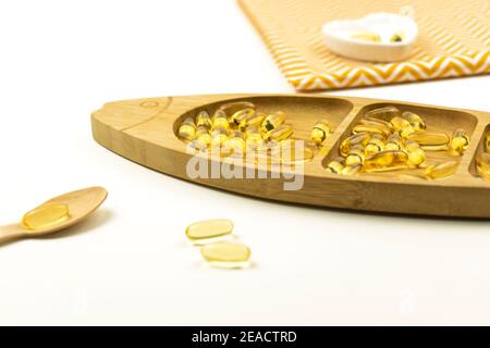 Le capsule gialle di Omega 3 giacciono su una piastra di legno sotto forma di pesce Foto Stock