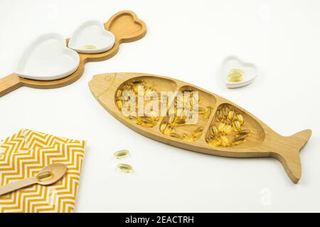 Le capsule gialle di Omega 3 giacciono su una piastra di legno sotto forma di pesce Foto Stock