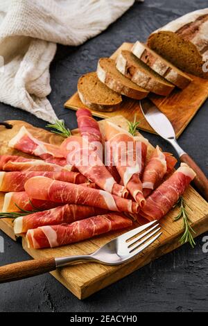 Fette di jamon arrotolate su tagliere di legno Foto Stock