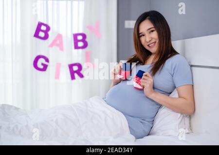 donna incinta con calzini per bambini su un letto Foto Stock