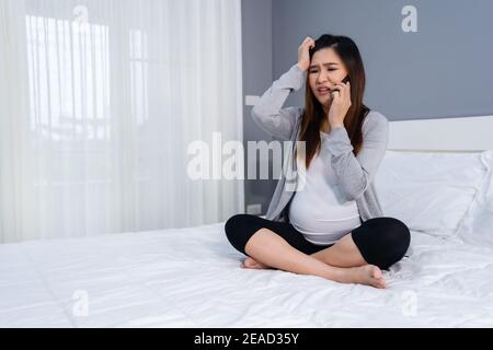 donna incinta stressata che parla su un telefono cellulare in un letto Foto Stock
