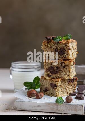 Quadrati di farinata d'avena con cioccolato e una tazza di latte, fondo di cemento chiaro. Dieta bar. Panetteria sana per colazione o dessert. Messa a fuoco selettiva. Foto Stock