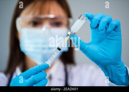 medico femminile che aspira il flacone di vaccino nel medicinale per iniezione con siringa Foto Stock