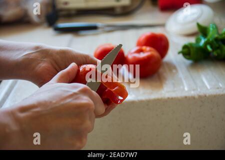 la donna sta sbucciando il pomodoro fresco con il coltello. la donna sposata sta tagliando i pomodori freschi e i peperoni. preparando un'insalata o un pasto