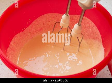 L'impasto viene preparato in una ciotola rossa con un mixer. Donna adulta cake deliziosi e croccanti biscotti in pandemia Foto Stock