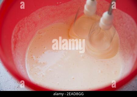 L'impasto viene preparato in una ciotola rossa con un mixer. Donna adulta cake deliziosi e croccanti biscotti in pandemia Foto Stock