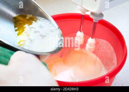 Il burro fuso viene aggiunto mentre si prepara l'impasto in una ciotola rossa con un miscelatore. Donna adulta cake deliziosi e croccanti biscotti in pandemia Foto Stock